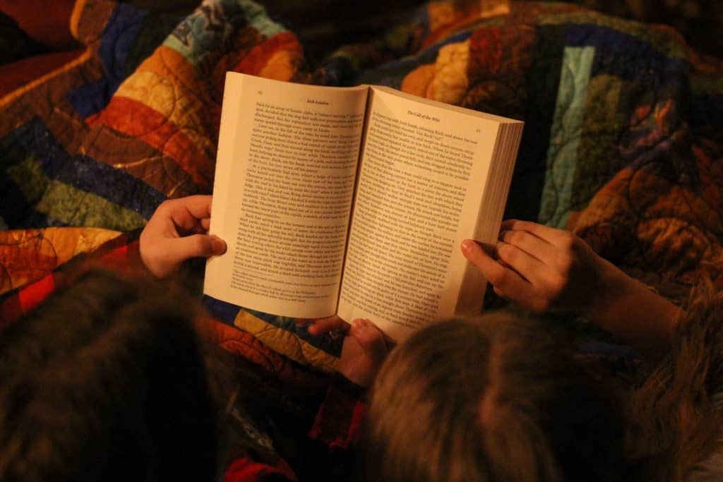 Two girls reading a book on a quilt.