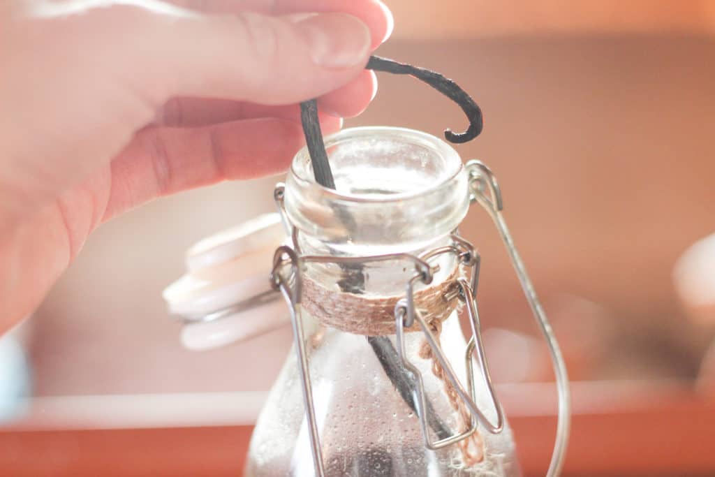 Hand placing vanilla bean into glass jar