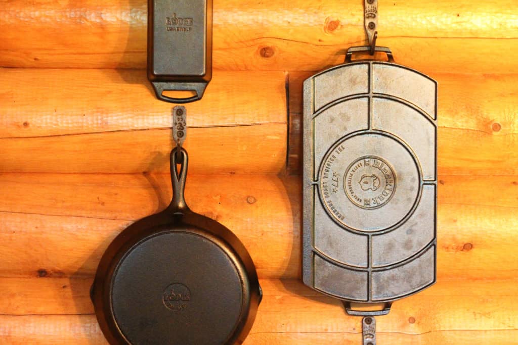 3 cast iron cookware pieces hanging on a log wall.