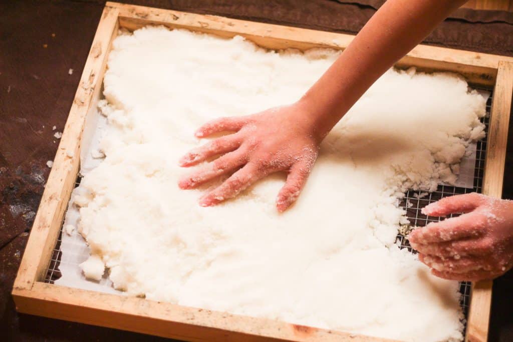 A hand patting sugar onto a candy board for bees to eat during winter.