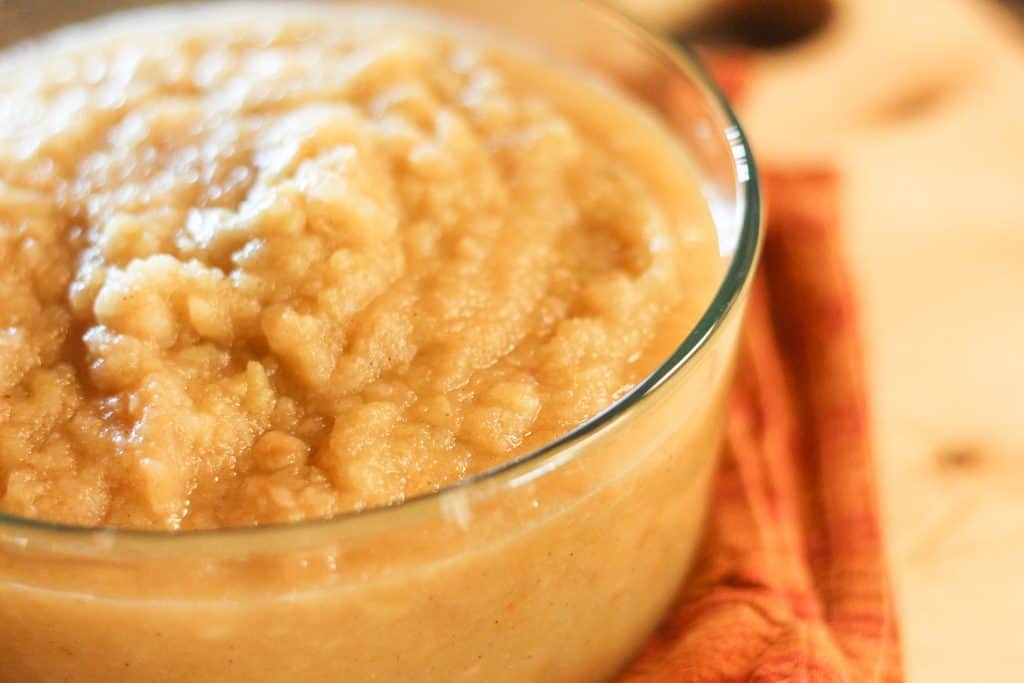 A glass container full of honey sweetened applesauce.