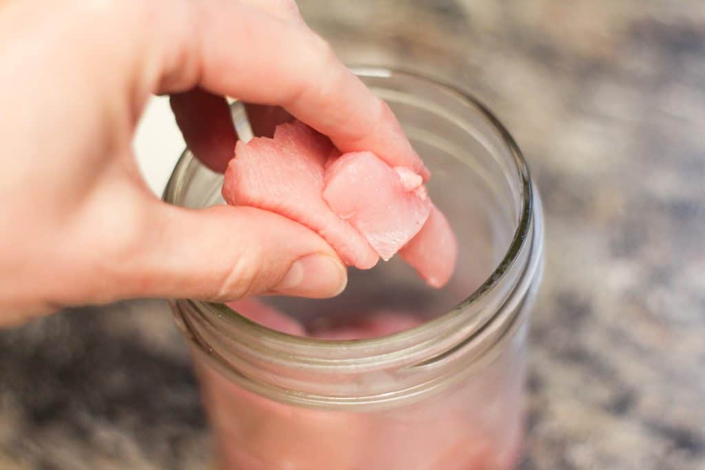 A hand placing turkey meat into a canning jar