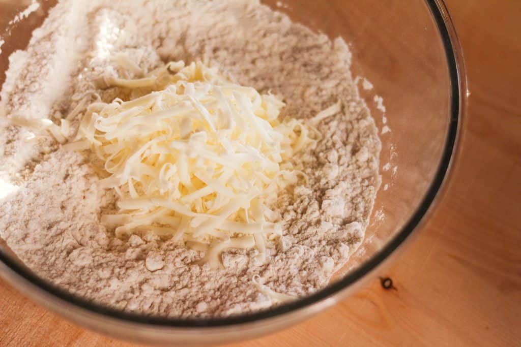 A bowl of flour with crumbled butter on top.