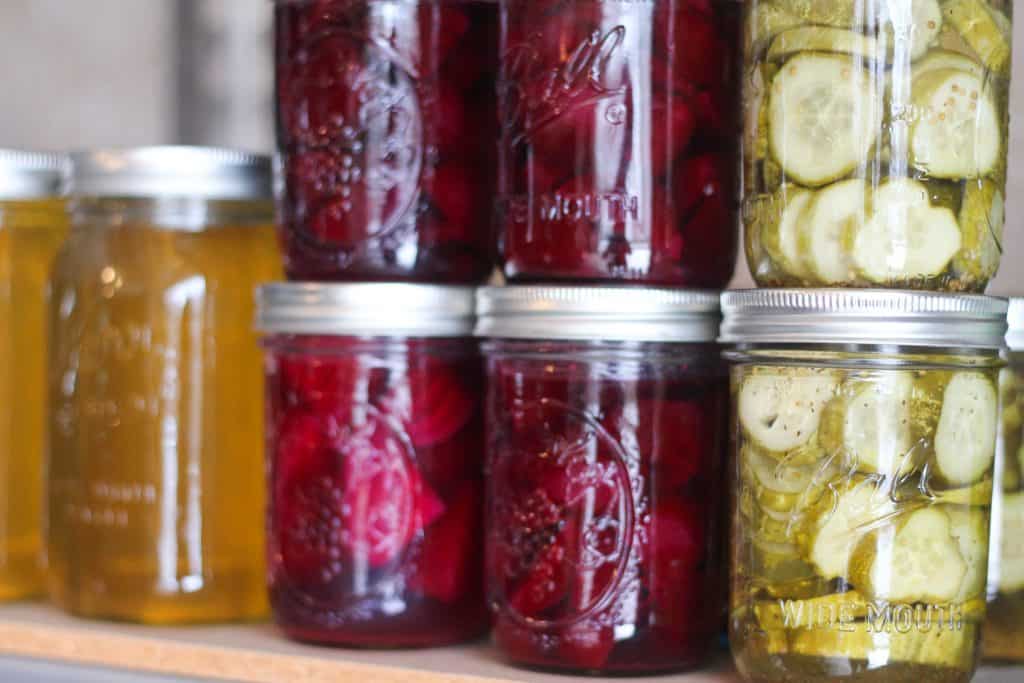 Home-canned foods in jars including pickled beets, honey, and dill pickles.