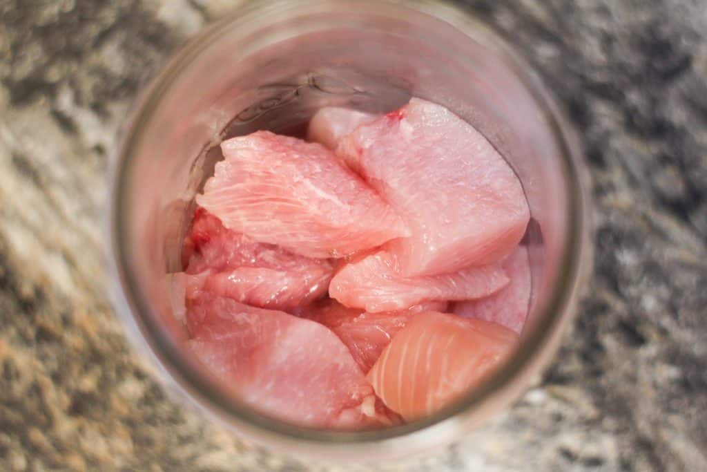 A glass canning jar with raw turkey meat