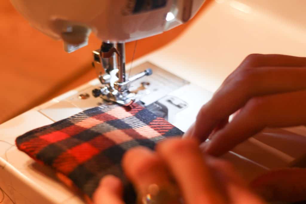 Hands pushing fabric through sewing machine