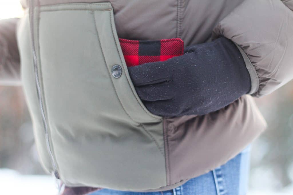 A gloved hand placing a hand warmer into a coat pocket