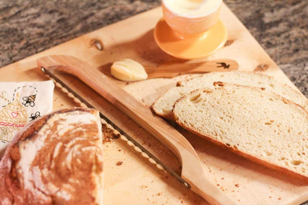 A wooden cutting board with a loaf of bread and a bread knife on it