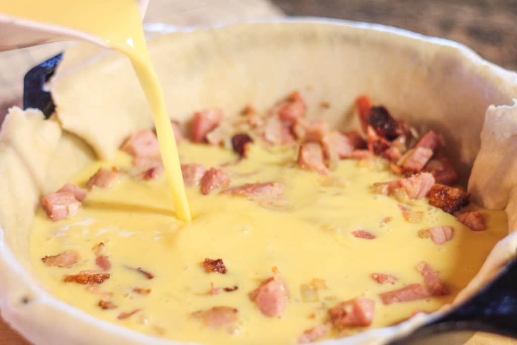 Eggs and milk being poured over the ham in the pie shell
