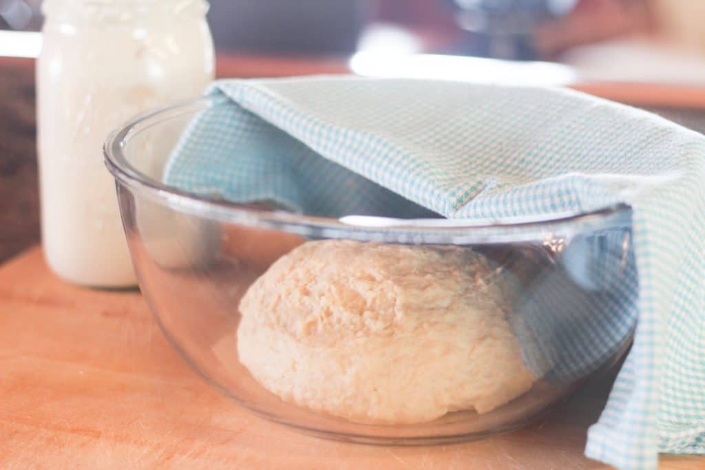 Glass bowl full of dough with towel on top