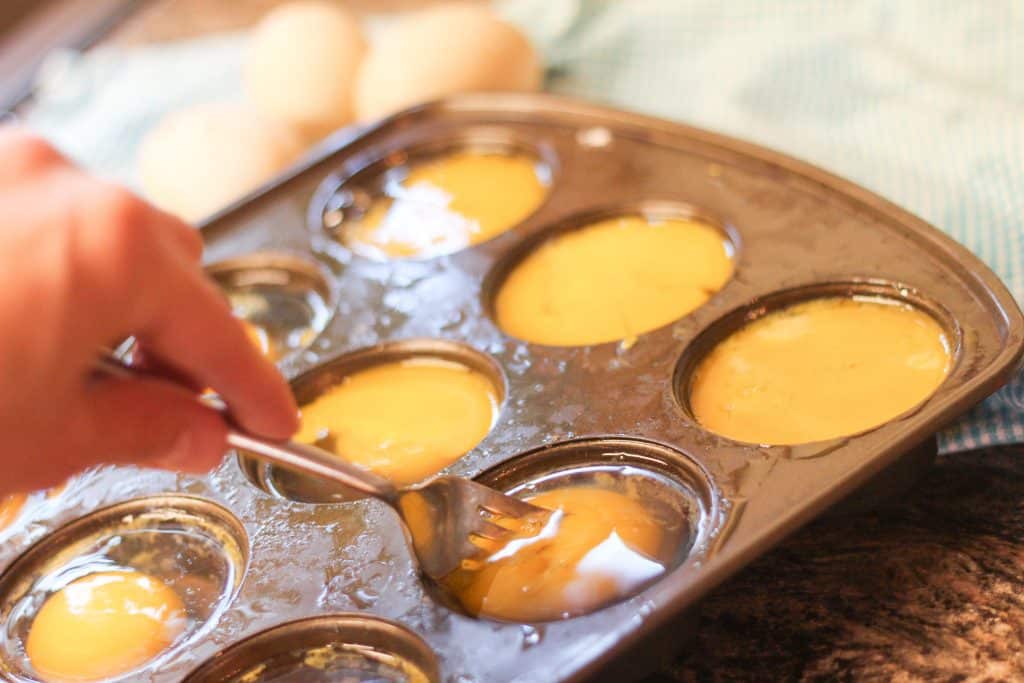 Eggs being cracked into a muffin tin and mixed with a fork