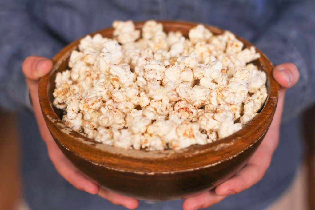 Hands holding a bowl of homemade popcorn with cinnamon sprinkled on top