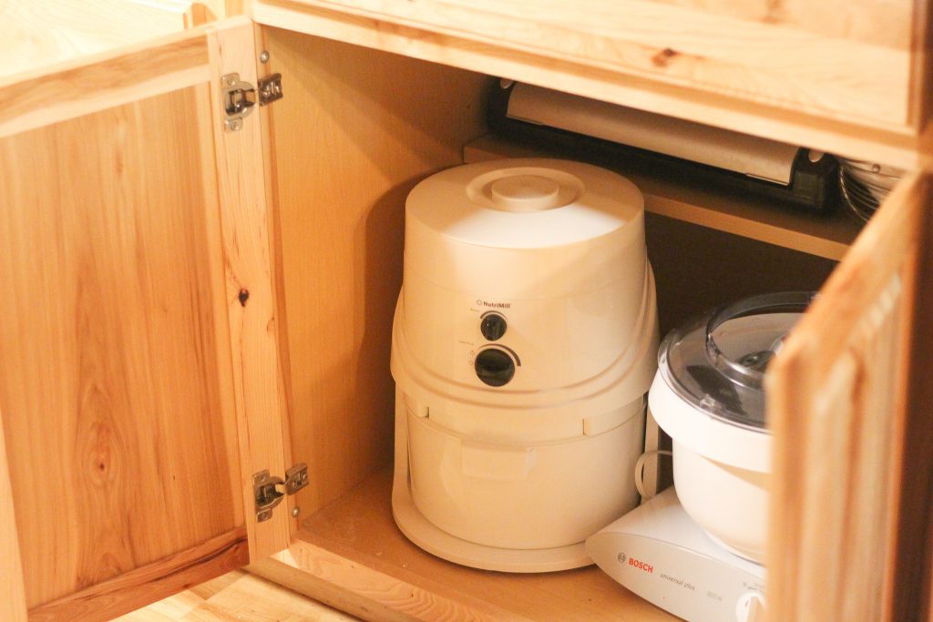 A kitchen cabinet opened with a grain mill in it