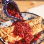 Homemade berry syrup being poured onto crepes