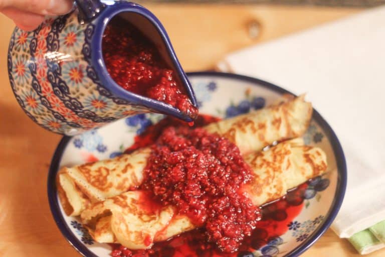 Homemade berry syrup being poured onto crepes