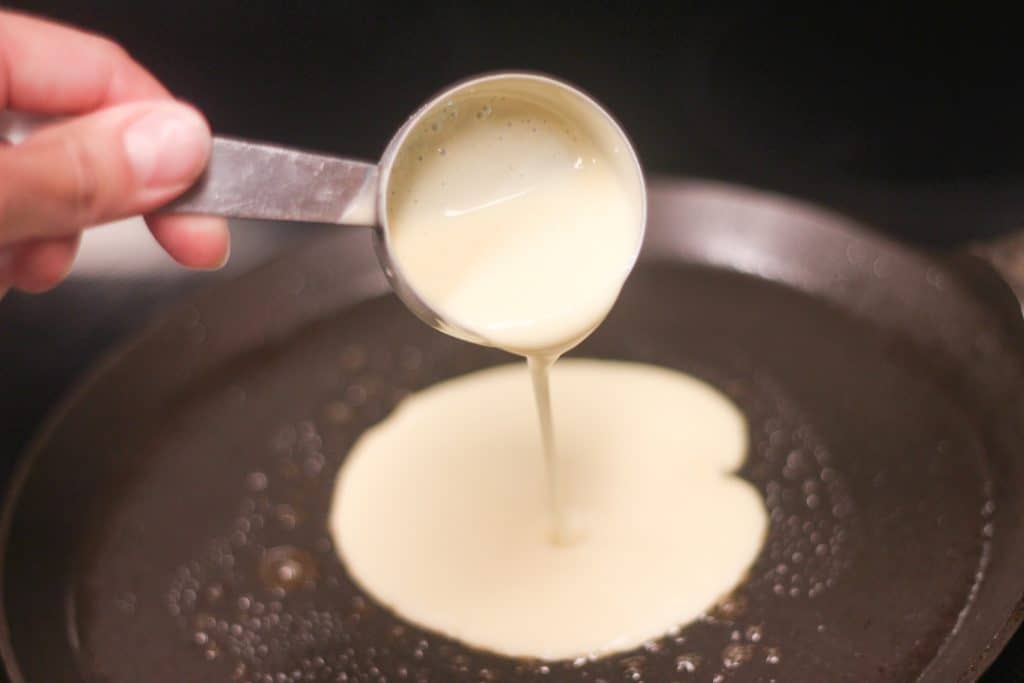 A measuring cup pouring batter onto a pan