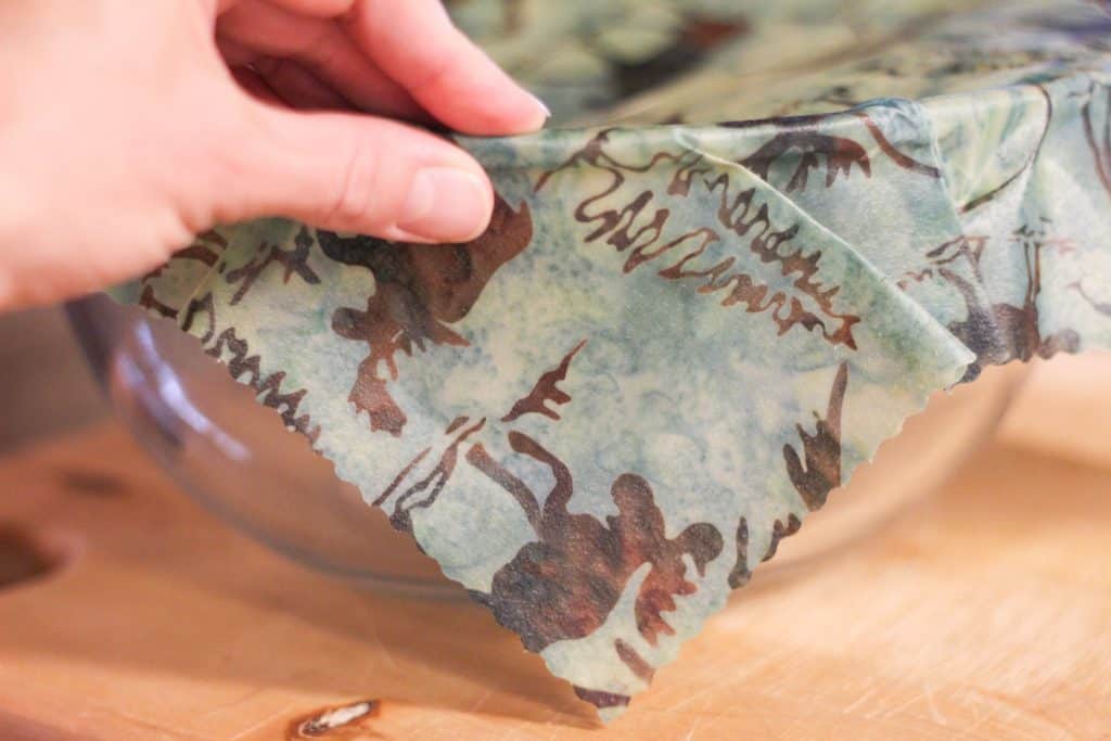A hand pinching beeswax wrap over the rim of a bowl