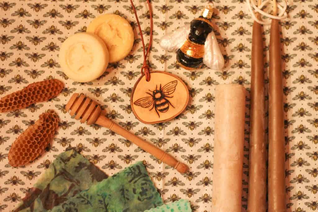 An image of some honey gift basket ideas, candles, a wooden honey dipper, beeswax wraps, two bee ornaments, and two lotion bars