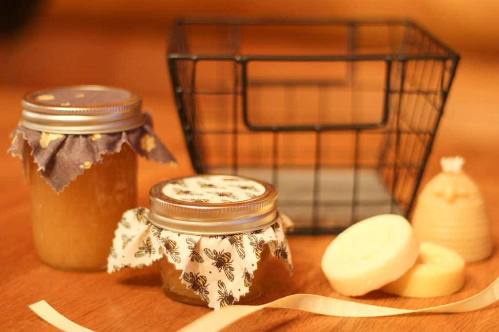 A black basket with two small jars of honey, a small candle, and two lotion bars sitting outside it