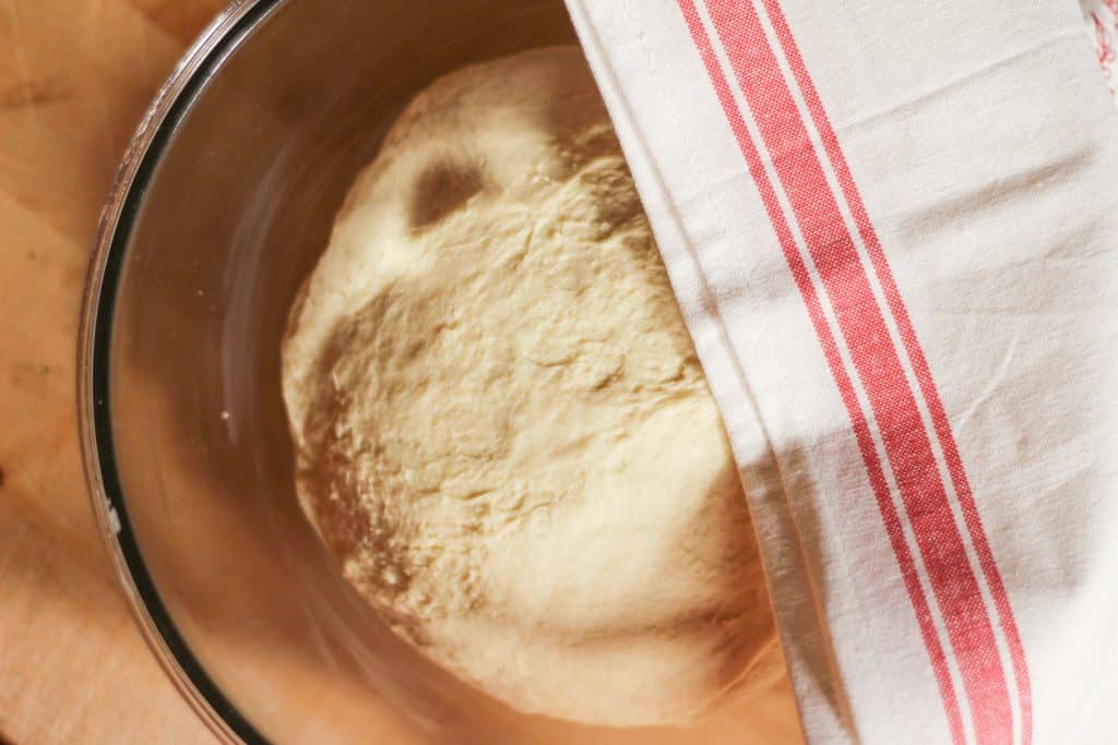 A ball of dough rising in a glass bowl covered with a towel