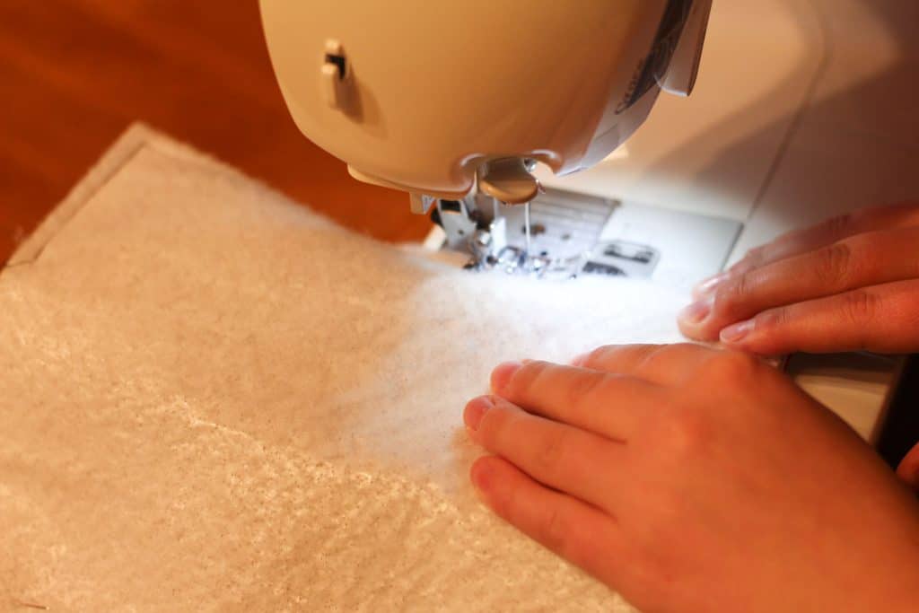 Hands pushing insulbrite and fabric through a sewing machine to sew the edges