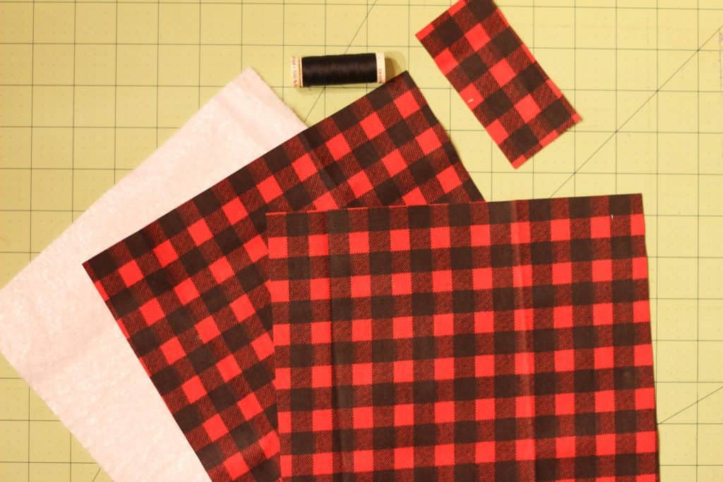 2 squares of fabric, a square of insulbrite, a small rectangle of fabric, and a spool of thread. Materials to make a pot holder