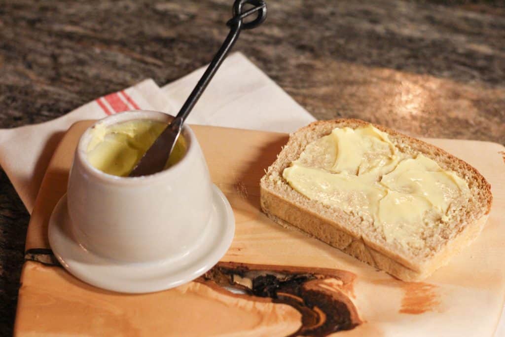 A slice of bread with butter on a top sitting next to a butter pot