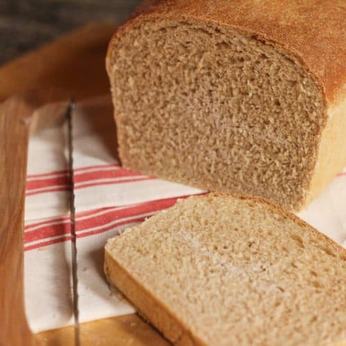 A loaf of whole wheat sourdough sandwich bread sliced on a cutting board