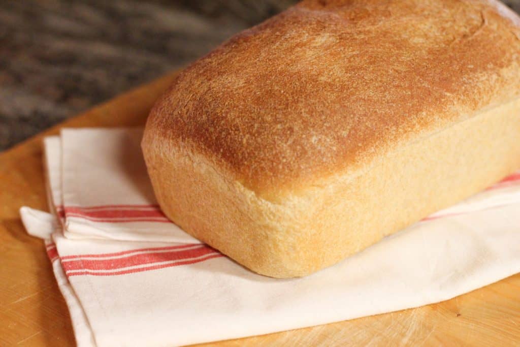 A baked loaf of whole wheat sourdough sandwich bread on a cutting board