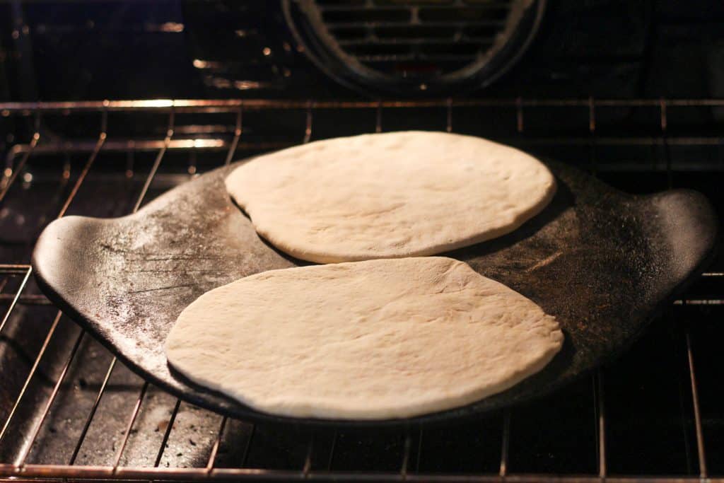 Two pieces of pita dough on a baking stone in an oven
