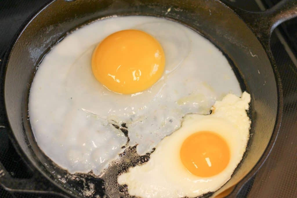 A goose egg and a chicken egg cooking in a skillet