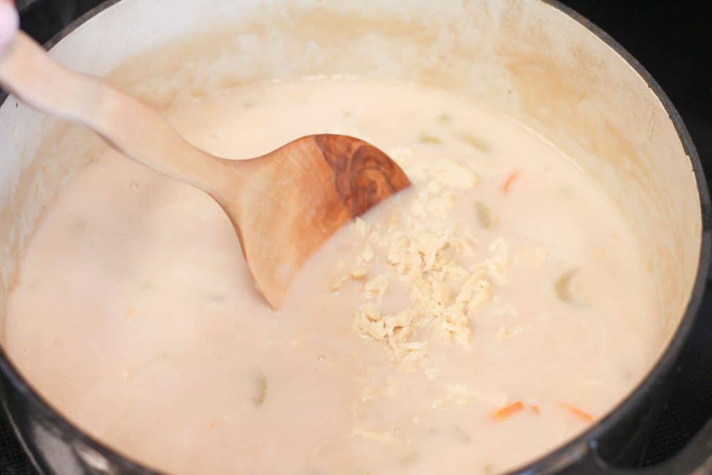 Shredded halibut being stirred into a pot of cooking chowder