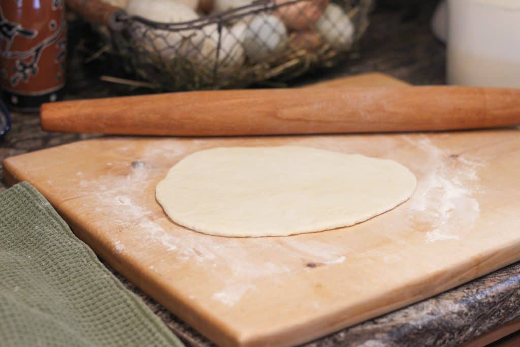 A piece of sourdough pita bread dough rolled out with a rolling pin