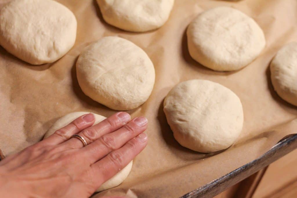 A hand flattening a ball of dough to make it into a hamburger bun shape