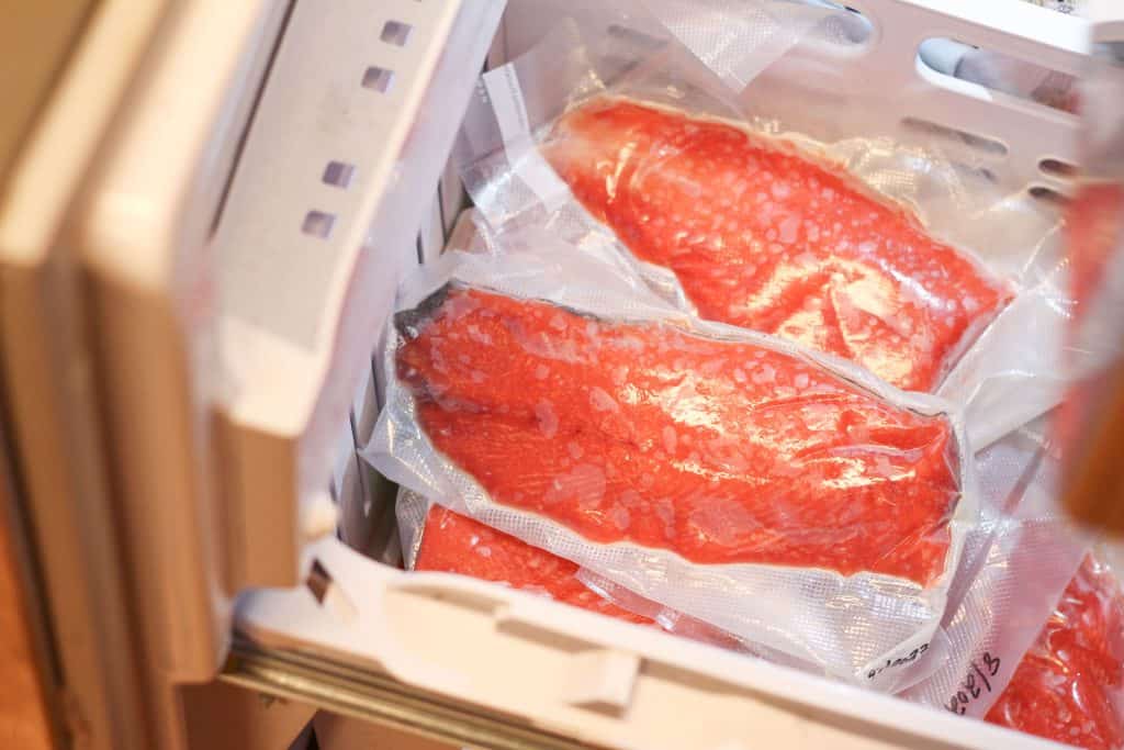 A freezer opened with packages of frozen salmon in it