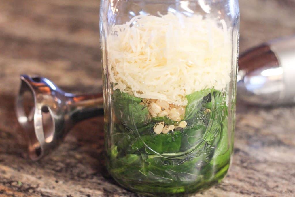 A glass jar full of homemade pesto ingredients, basil, parmesan cheese, pine nuts, olive oil